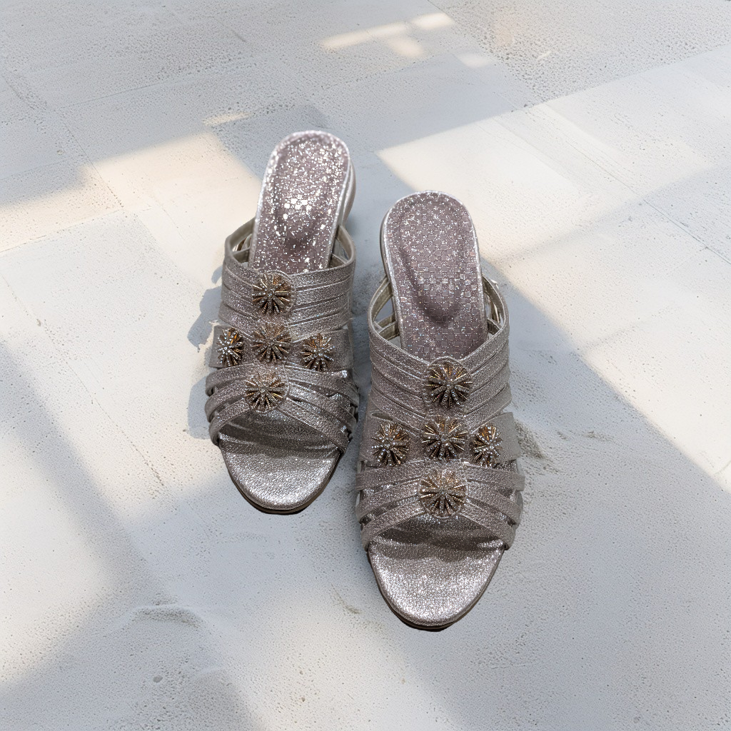 Pair of silver glittery sandals with decorative flowers on a light surface